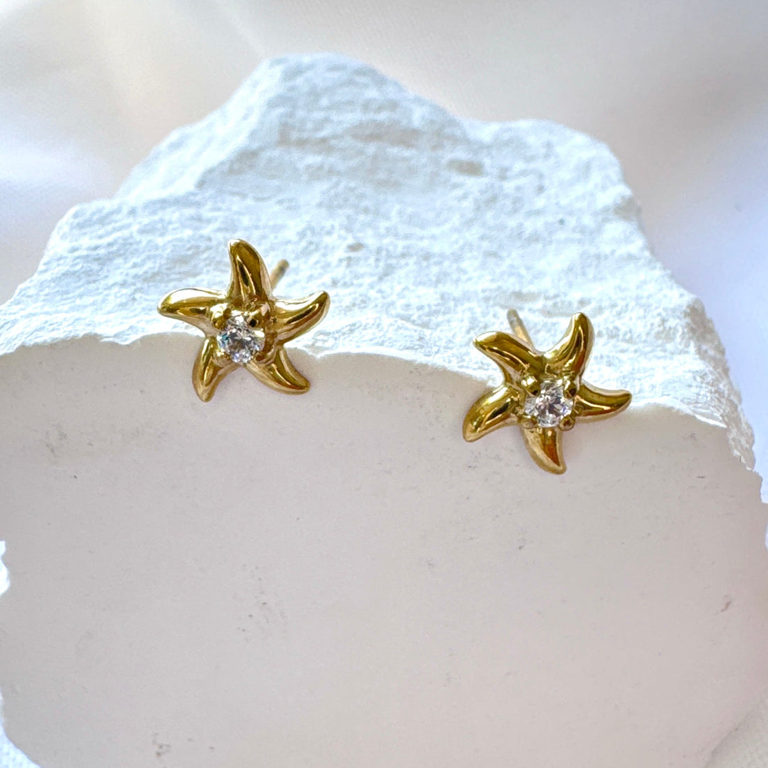 Gold starfish earrings with clear stones on a white stone background
