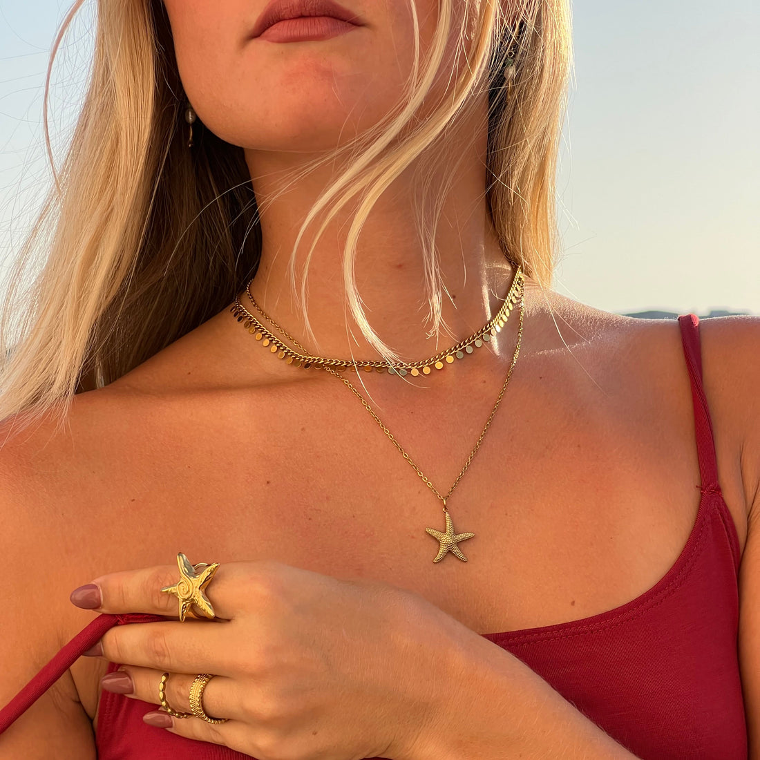 Woman in a red swimsuit with starfish-themed jewelry on a beach.