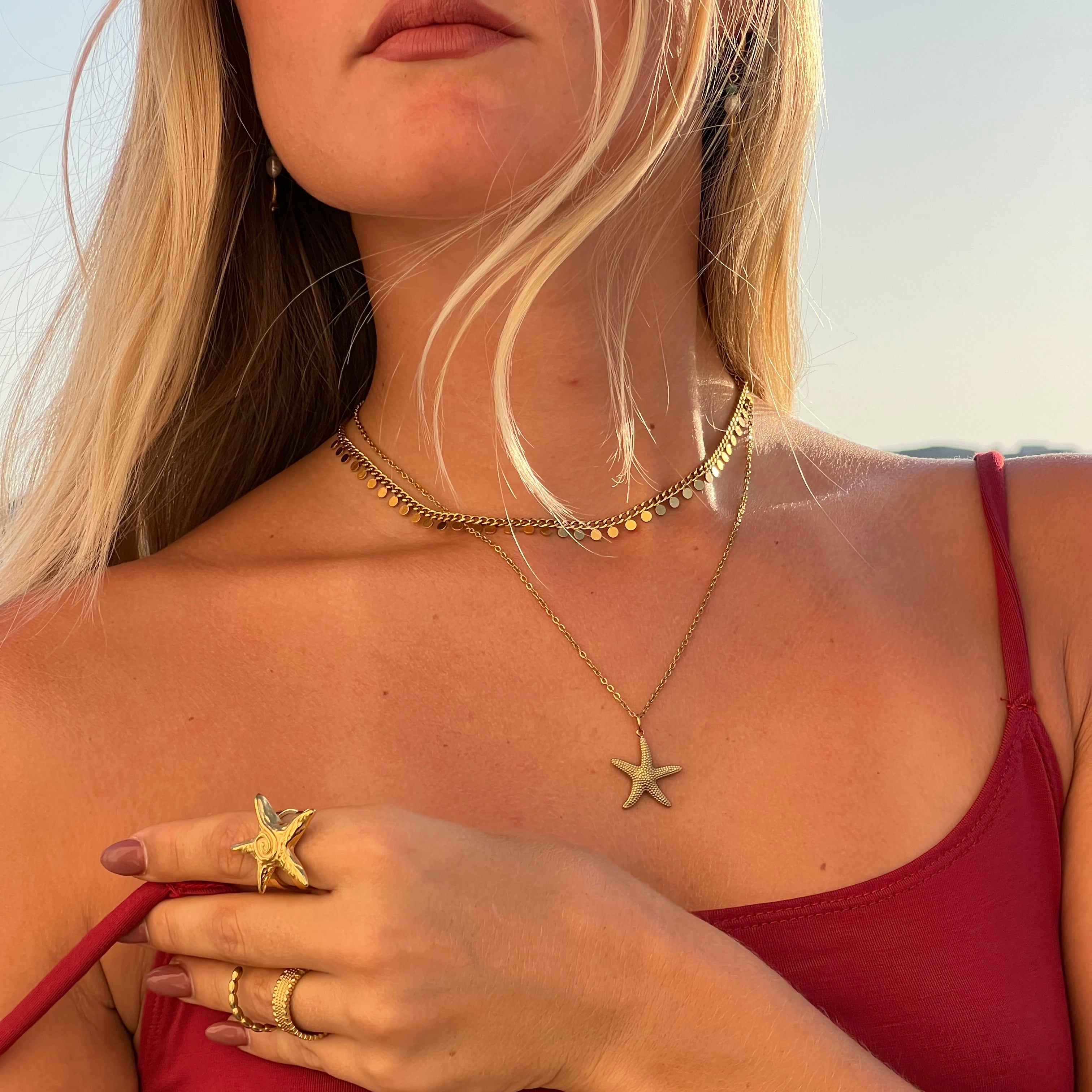Woman in a red swimsuit with starfish-themed jewelry on a beach.