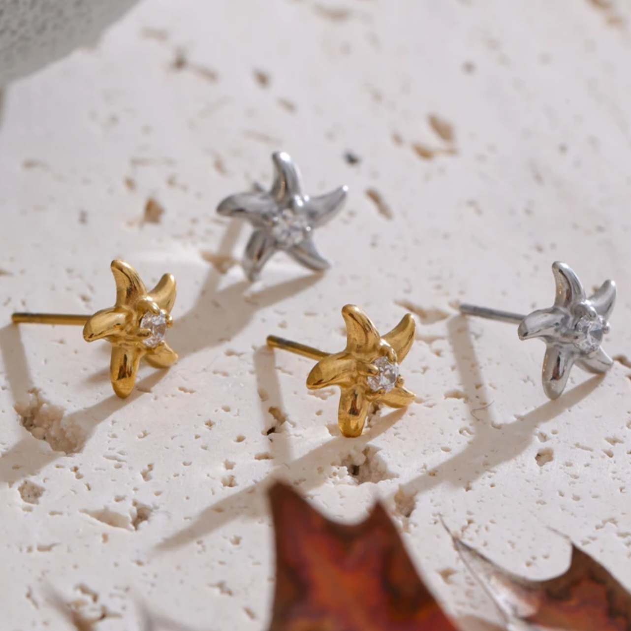 Pair of starfish-shaped earrings in gold and silver on a textured surface